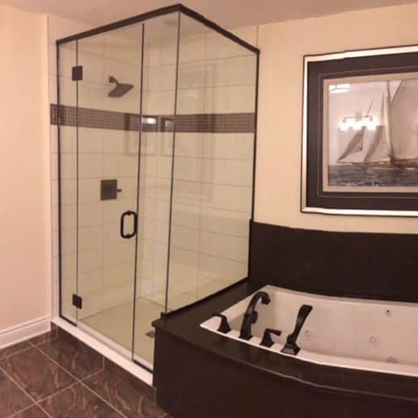 Glass shower with black hardware beside bathtub
